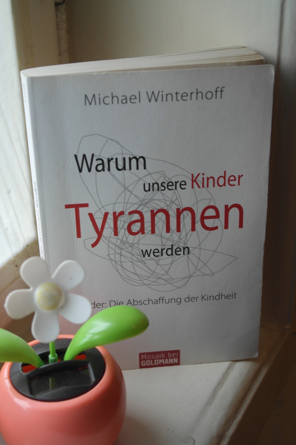 Das Bild zeigt ein Buch und eine Kunstpflanze